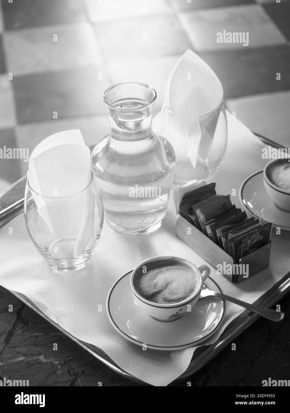 Venedig, Italien - 30. Juni 20220 Schwarzweißfoto eines Tabletts mit einer dampfenden Tasse Kaffee, einer Wasserkaraffe, Zuckerpackungen und leeren Gläsern in A Stockfoto