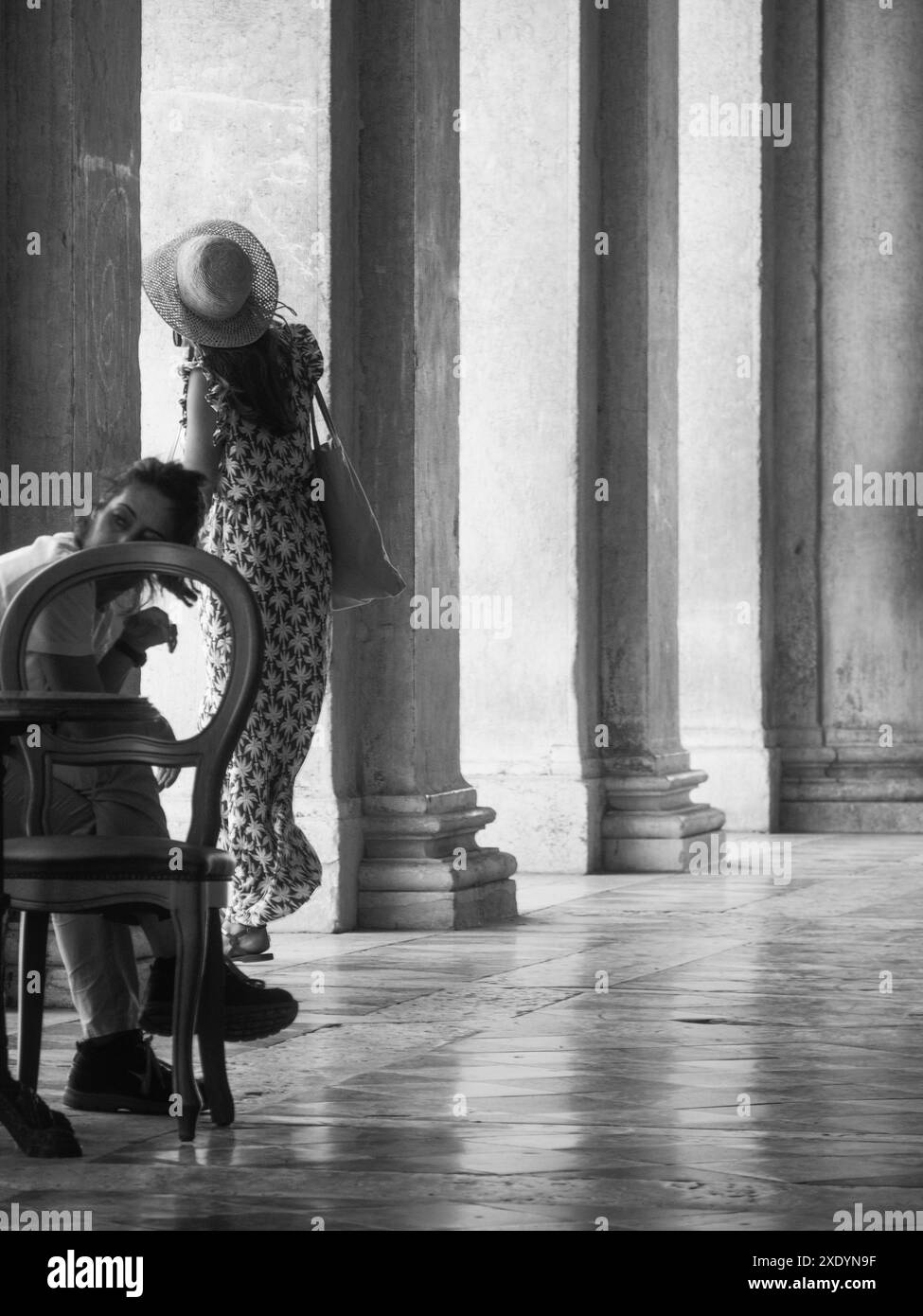 Venedig, Italien - 30. Juni 20220 Mann schläft auf einem Stuhl, während sich eine Frau zwischen Säulen im Schatten umsieht Stockfoto