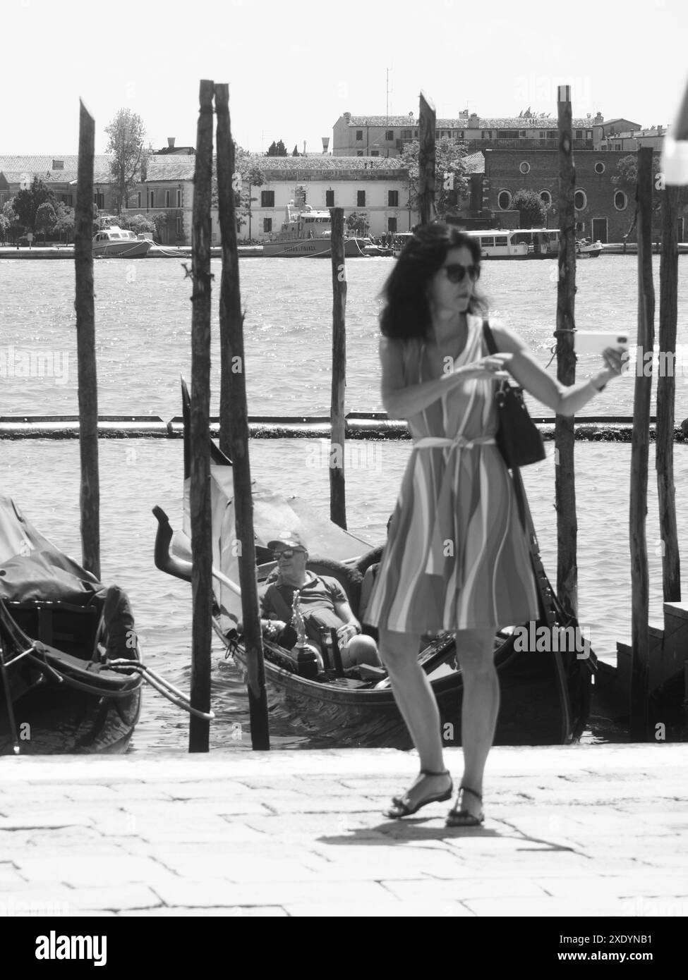 Venedig, Italien - 30. Juni 20220 Frau, die ein Selfie mit ihrem Smartphone macht, während sie von einem Gondoliere weggeht, der auf Kunden in venedig, italien, wartet Stockfoto