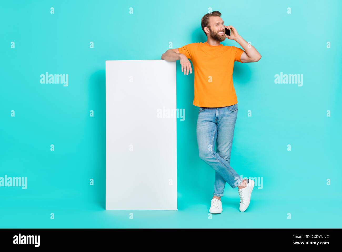Großes Foto von freundlichem Bart Guy Talk Phone Tragen Sie T-Shirt Jeans Schuhe isoliert auf blaugrün Hintergrund Stockfoto