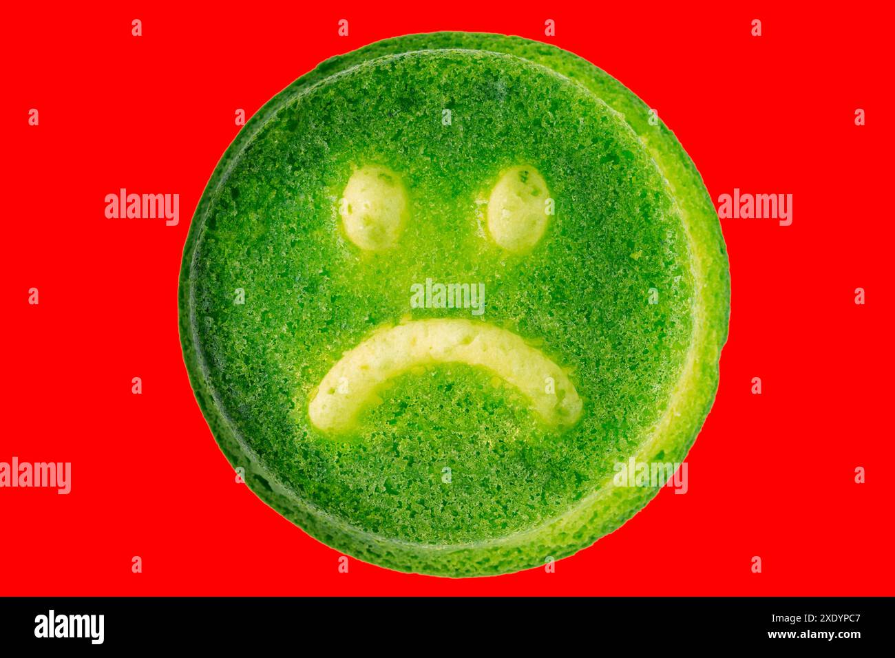 Unglücklicher Kekse mit grünem Gesicht isoliert auf rotem Hintergrund in flacher Lay-Perspektive Stockfoto