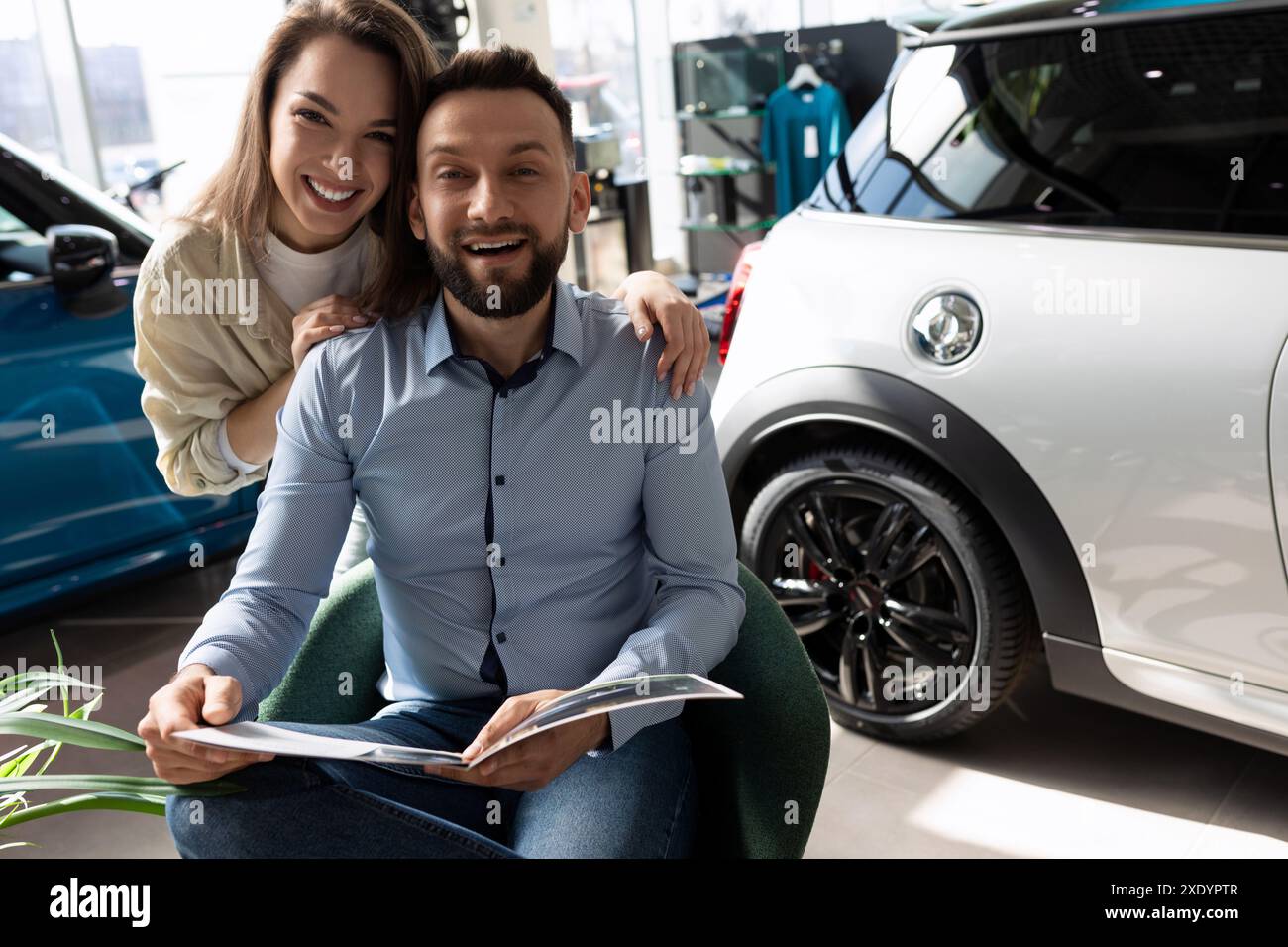 Ein junges verheiratetes Paar, das ein Heft studiert, bevor er ein neues Auto kauft, das Konzept der persönlichen Transportversicherung Stockfoto