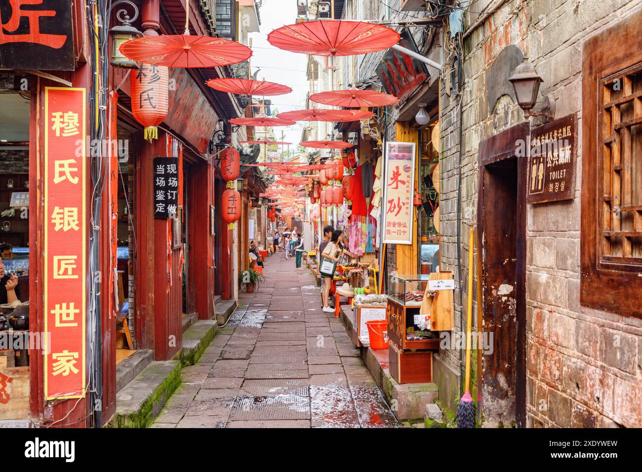 Fenghuang, China - 23. September 2017: Herrlicher Blick auf die gemütliche, enge Straße, die mit traditionellen orientalischen chinesischen roten Regenschirmen dekoriert ist. Stockfoto