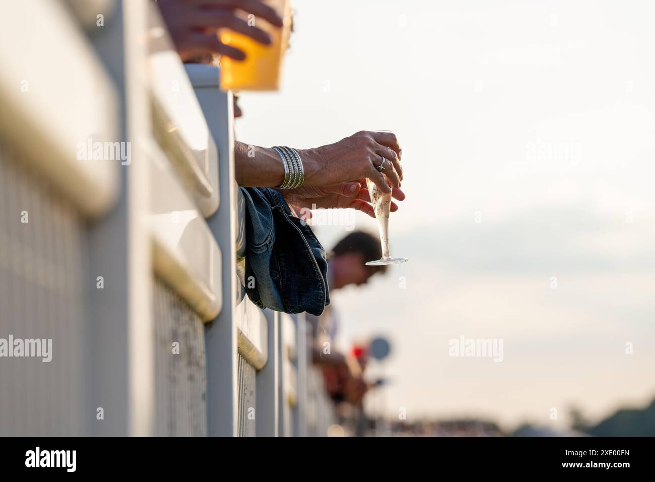 Hände, die Bier und Weingetränke halten, lehnen sich bei einem Wettkampf bei Tageslicht auf eine Barriere Stockfoto
