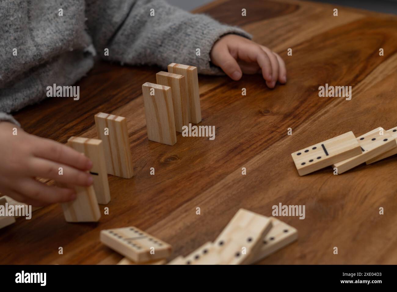 Kinderhände in grauem Pullover spielen Dominosteine mit verschwommenem Fokus Stockfoto