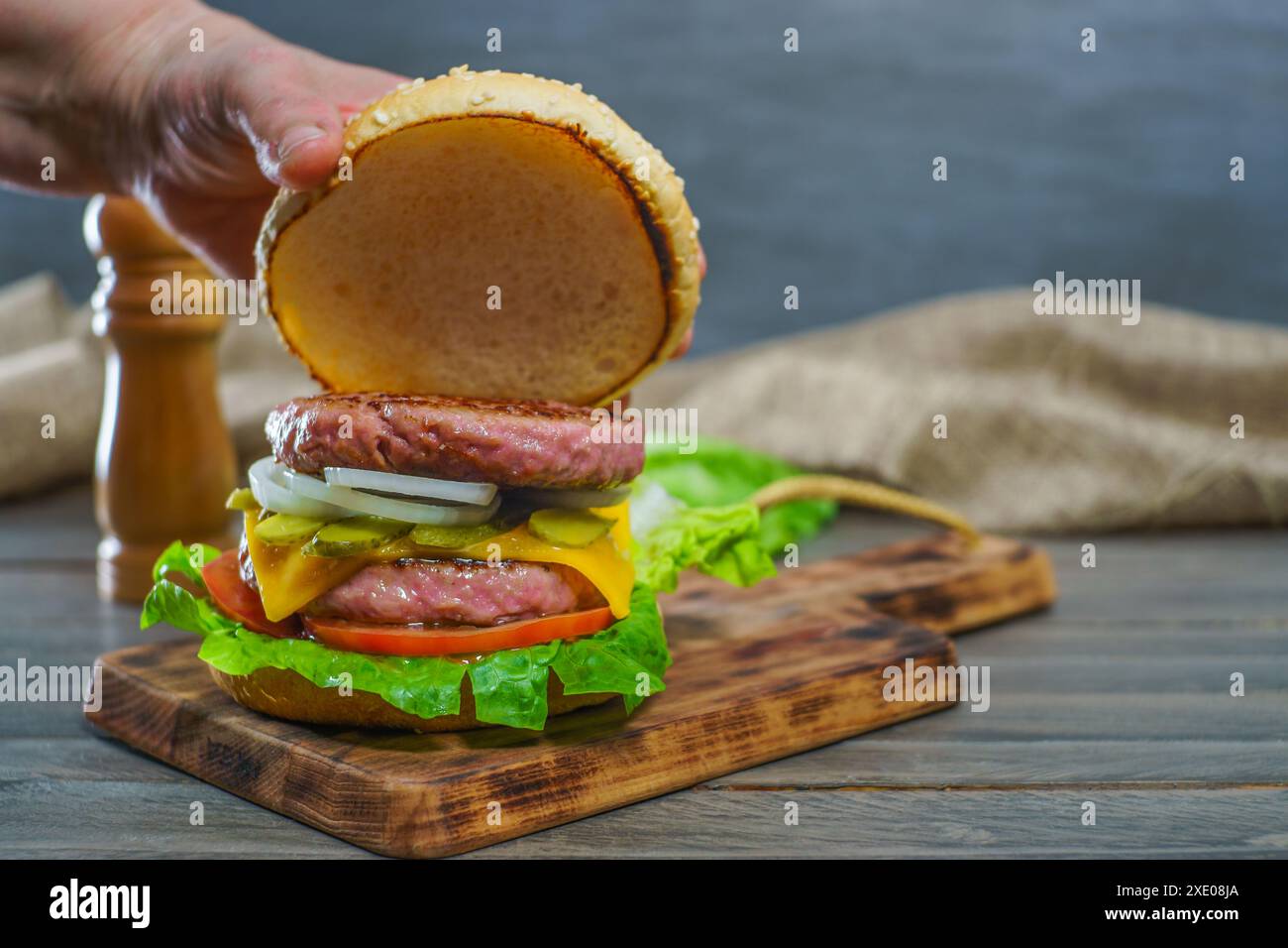 Frau, die das Brötchen eines Hamburger Brötchens öffnet, komplett mit zwei Fleischstücken Stockfoto