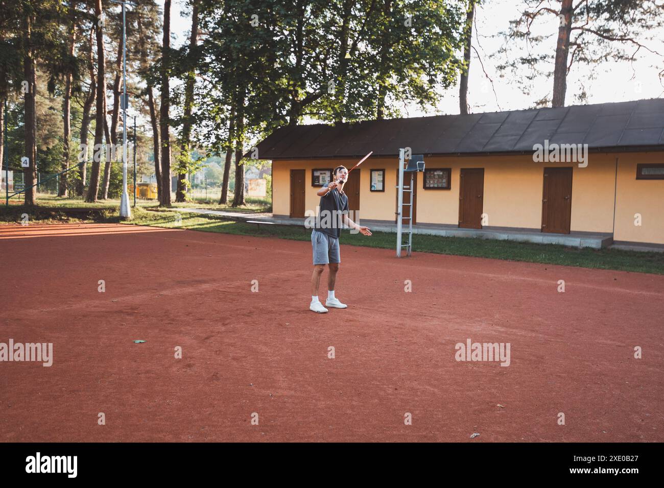 Ein schwarzhaariger Athlet mit einem Lächeln im Gesicht spielt Badminton auf einem Tonplatz. Begeisterung für den Amateursport. Lernen neuer Bewegungsfähigkeiten. Stockfoto