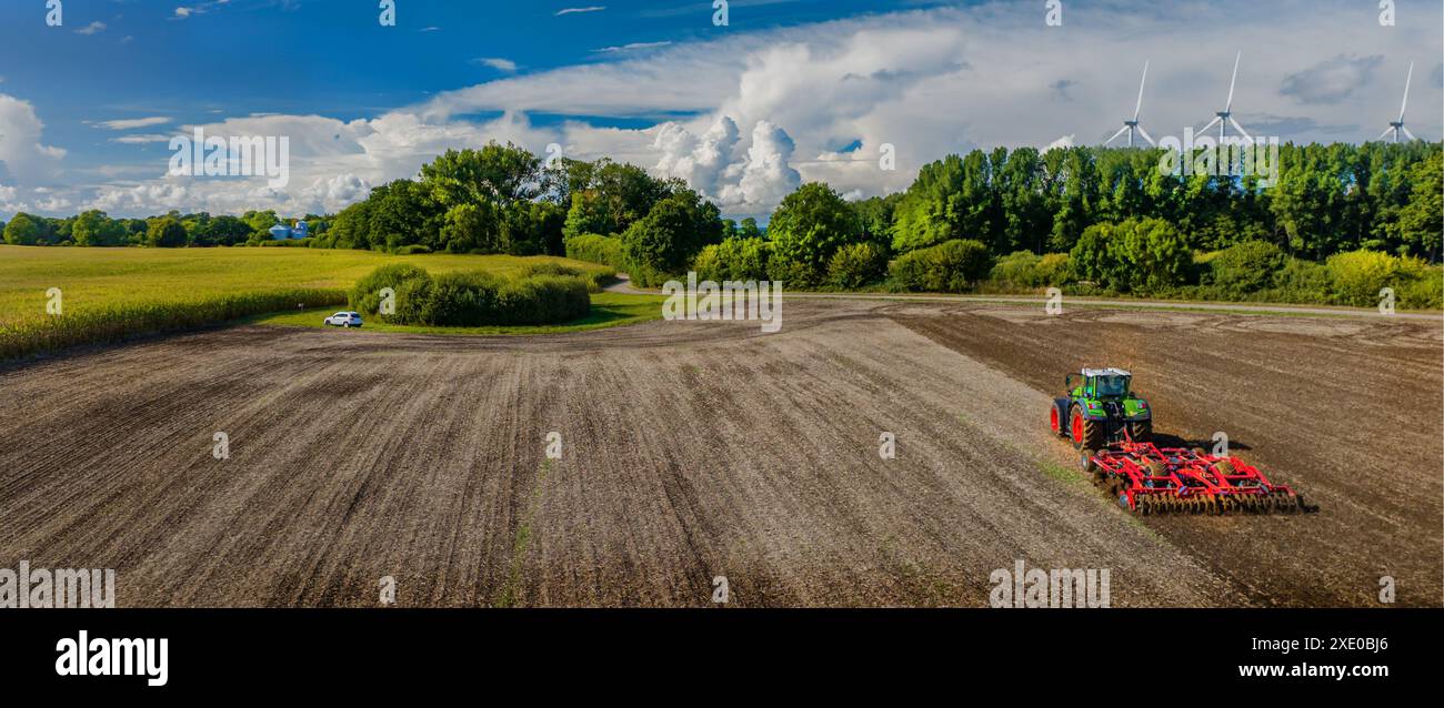 Luftaufnahme des landwirtschaftlichen Traktorpflügens auf einem Ackerfeld mit einem Windpark im Hintergrund. Stockfoto