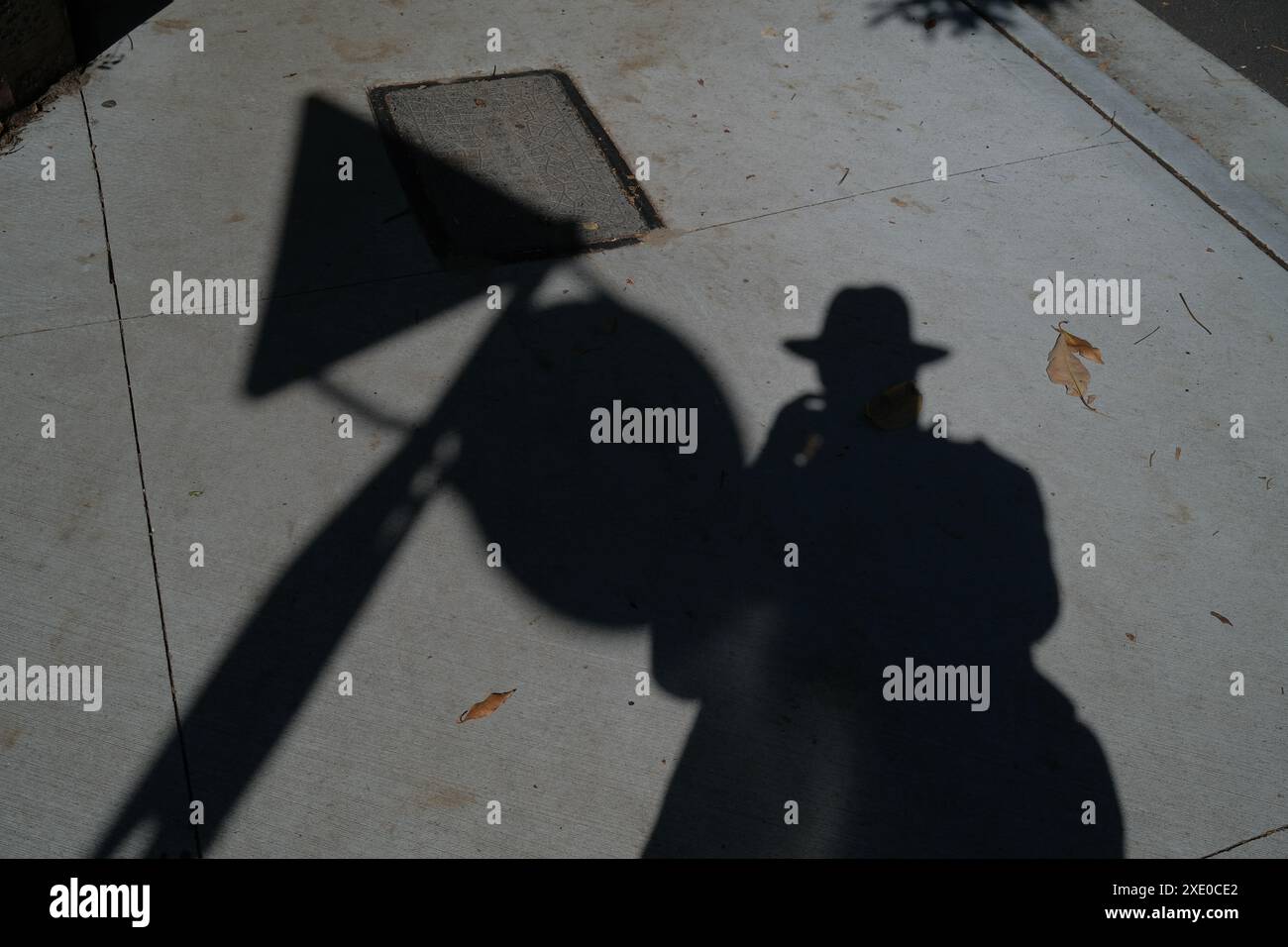 Schatten eines Mannes mit Fedora-Hut, gegossen auf einem Betonpflaster mit Kreis- und Dreiecksschatten auf einem hellgrauen Fußweg in Sydney Stockfoto
