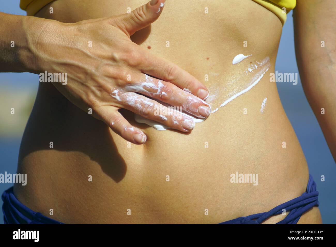 Ein Mädchen spreizt Sonnencreme über ihren Bauch - Nahaufnahme Foto. Frau am Strand schützt ihre Haut vor der Sonne. Stockfoto