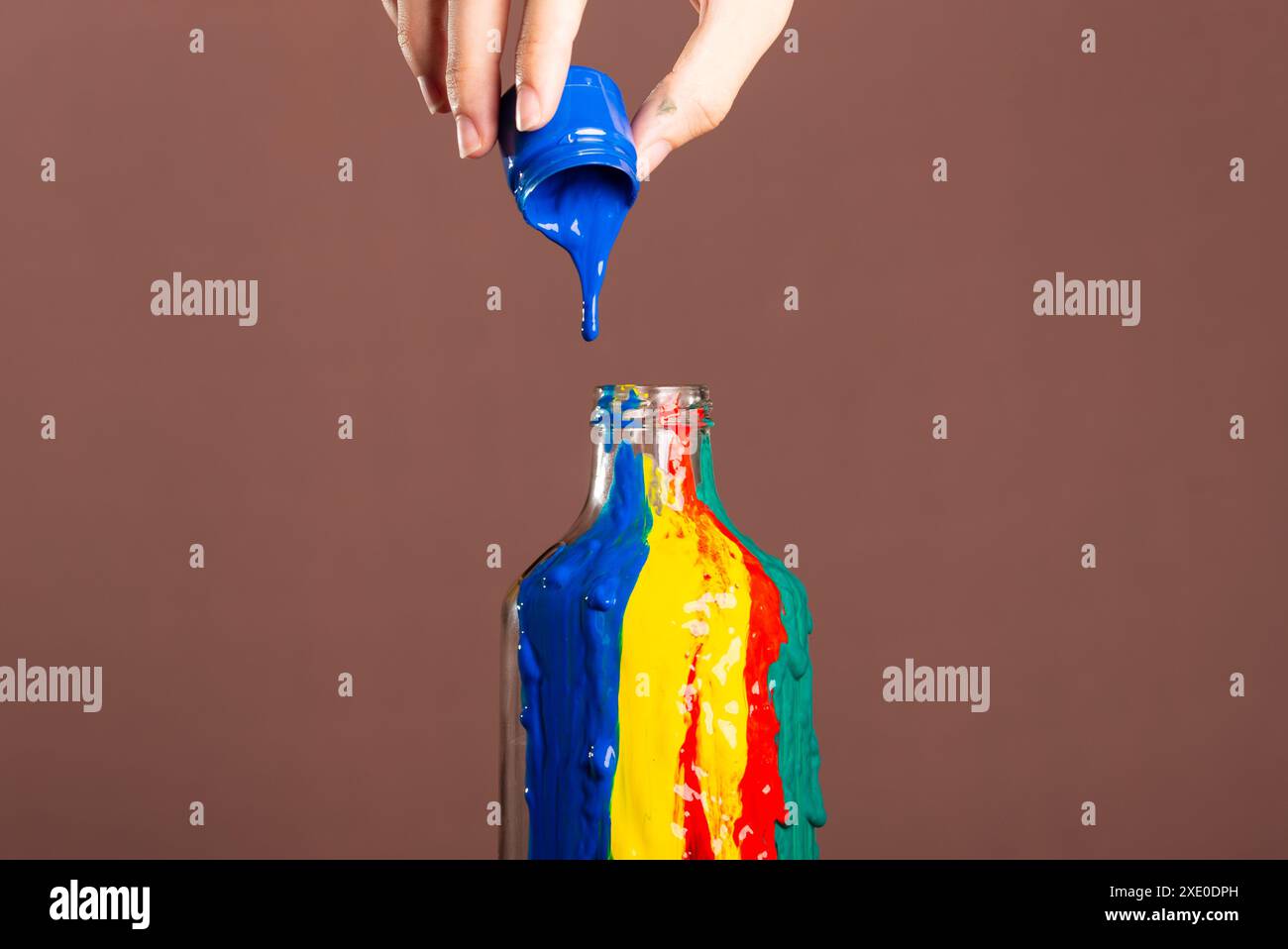 Maler gießen blaue Farbe von Hand in eine Glasflasche. Abstrakte Kunst. Isoliert auf braunem Hintergrund. Stockfoto