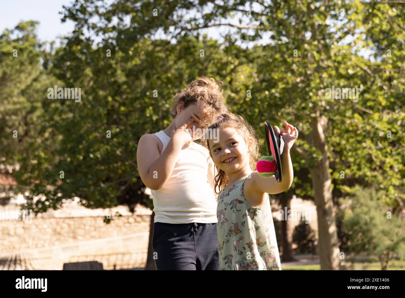 Der große Bruder und die kleine Schwester lächeln mit schelmischen Gesten und genießen Spiele in einem sonnigen Park. Fängt brüderliche Komplizenschaft und Freude an einem warmen Tag ein. Stockfoto