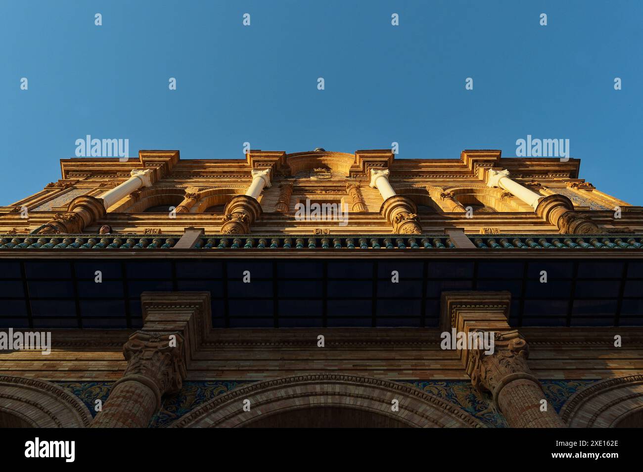 Blick nach oben auf die verzierte Fassade der plaza de España in Sevilla, mit komplexen architektonischen Details und Säulen vor einem klaren blauen Himmel Stockfoto
