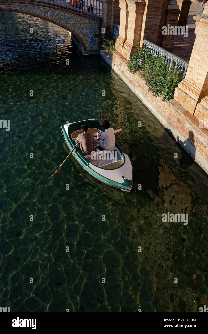 Zwei Personen rudern mit einem Boot auf dem Kanal der Plaza de España in Sevilla, deren Schatten auf die historischen Backsteinmauern geworfen werden Stockfoto