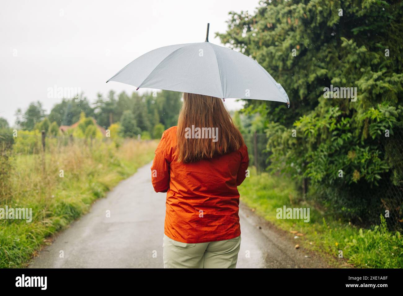 Porträt eines fröhlichen, schönen Mädchens, das mit Regenschirm unter Regen steht und nach Herbstregen lächelt Stockfoto