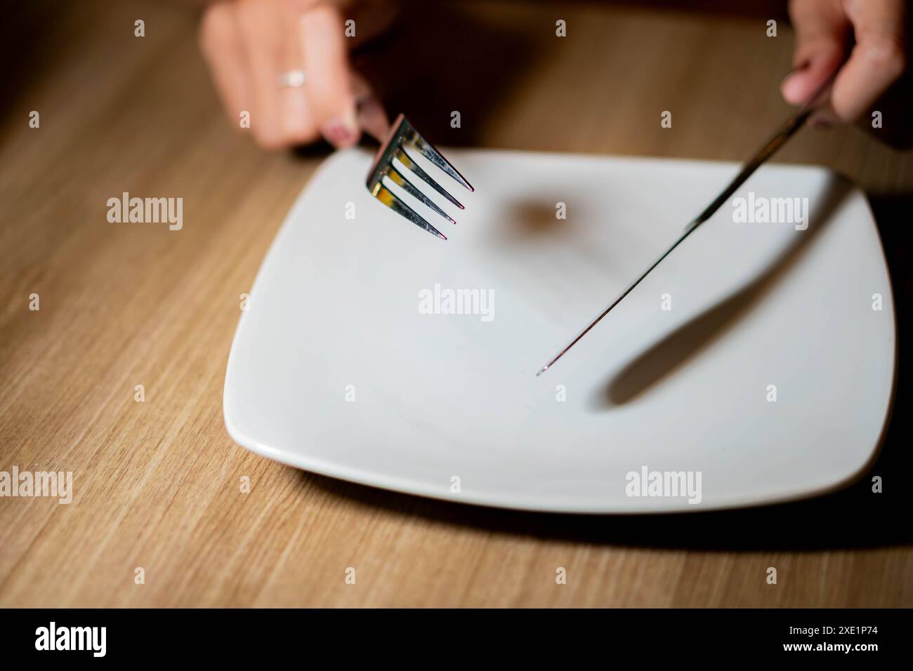 Eine Person, die eine Gabel und ein Messer über einem leeren weißen Teller hält und sich auf das Essen vorbereitet. Stockfoto