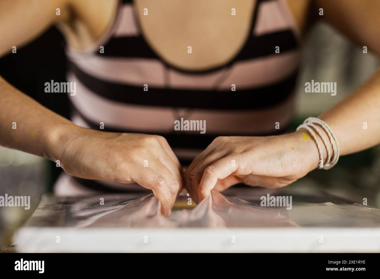 Eine Nahaufnahme der Hände einer Künstlerin, während sie sorgfältig eine Leinwand auf ihrem Arbeitsplatz anpasst und dabei Konzentration und Handwerkskunst zum Ausdruck bringt. Stockfoto