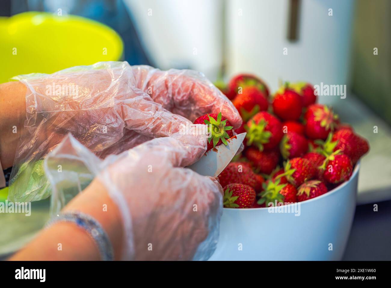 Nahaufnahme von mit Handschuhen versehenen Frauenhänden, die Erdbeeren mit Messer in der Hausküche reinigen. Stockfoto