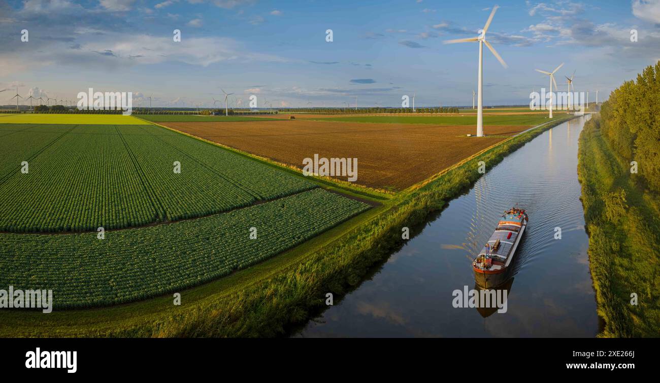 Landwirtschaftliche Flächen entlang des Kanals mit Booten, die sich auf dem Kanal bewegen, und Reihe rotierender Windturbinen entlang des Verbots Stockfoto
