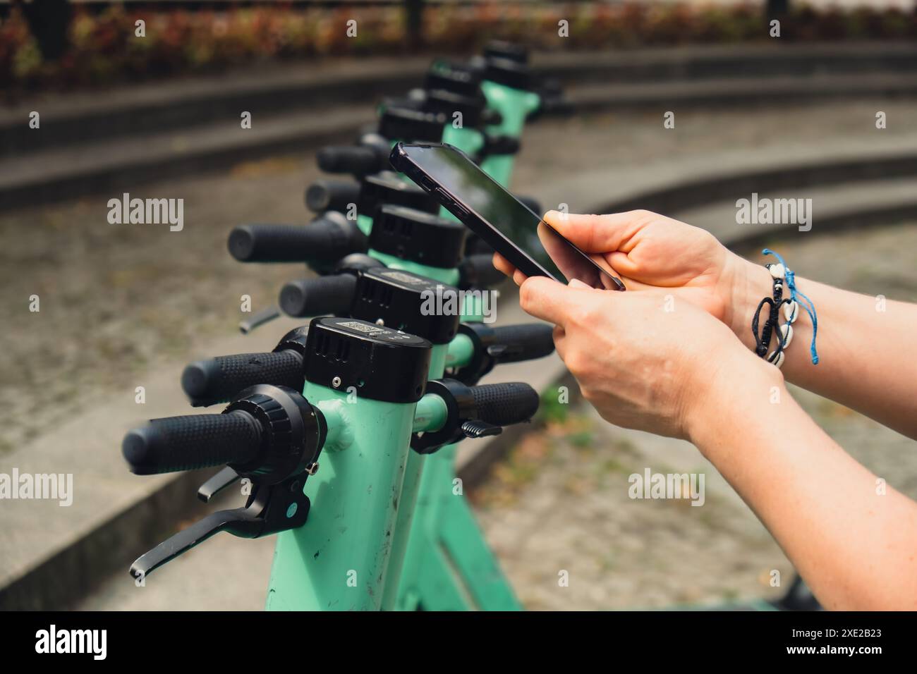 Weibliche Hand verwendet Mobiltelefon, um QR-Code auf Elektroroller auf der Straße auf E-Scooter, Mietservice-App zu scannen. Alternative tr Stockfoto