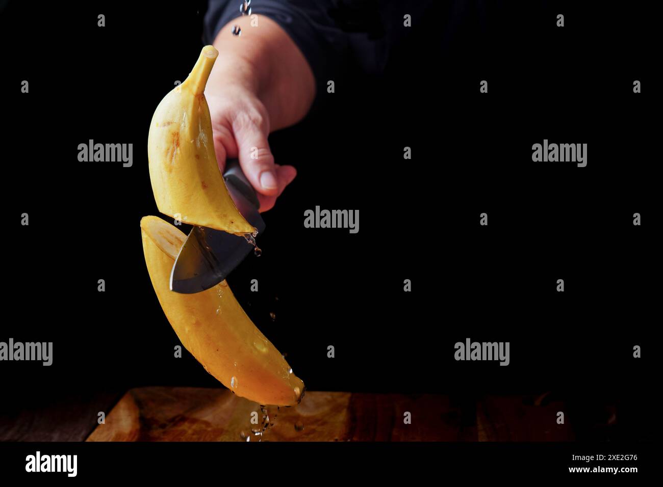 Frau, die eine Banane halbiert, mit einem Messer in der Luft Stockfoto