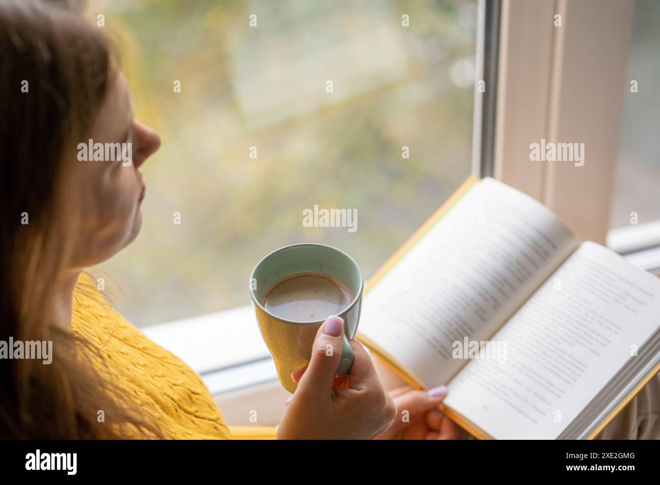 Junge schöne Frau in der Nähe des Fensters gelber Strickpullover Lesen Buch Stockfoto