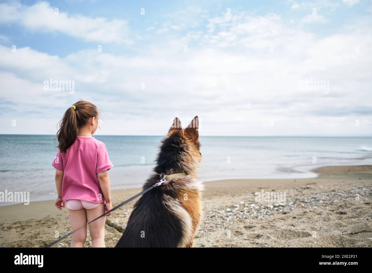 Ein Mädchen in einem rosafarbenen T-Shirt und ein Hund schauen aufs Meer. Stockfoto