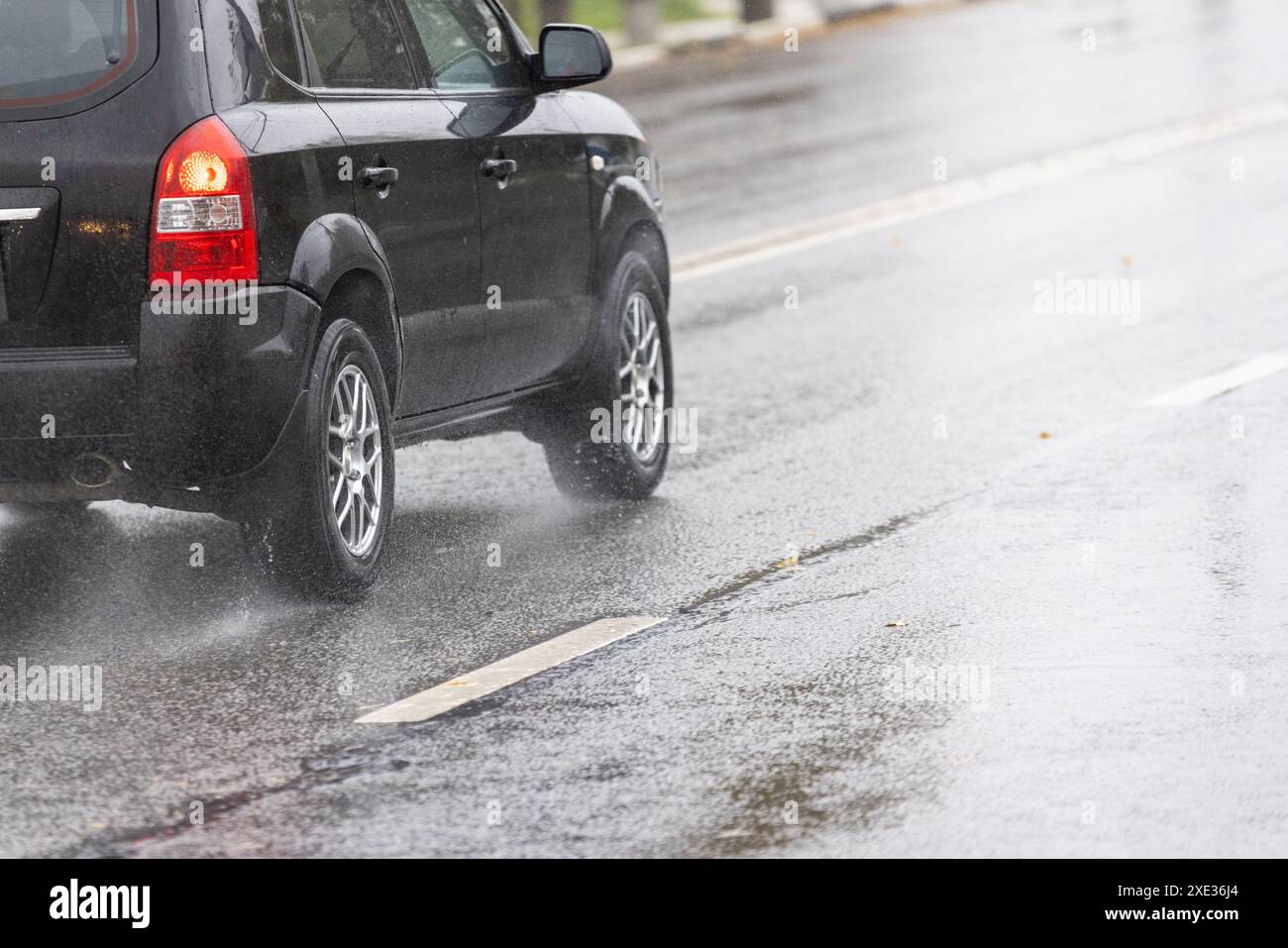 Regen Wasser spritzt von den Rädern des schwarzen SUV, die sich schnell auf Asphaltstraßen bewegen Stockfoto