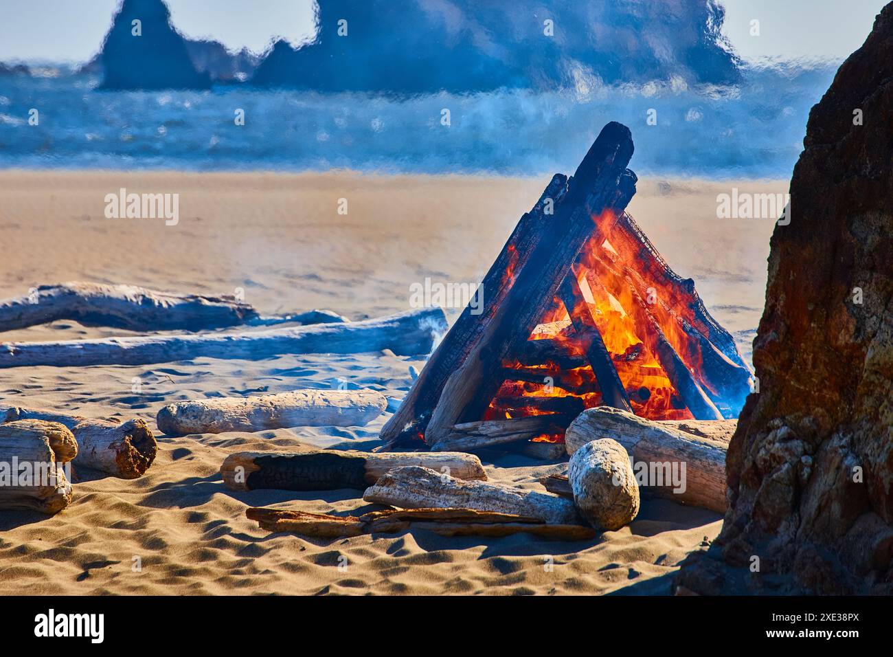 Lagerfeuer am Strand bei Sonnenuntergang mit Blick auf das Meer aus der Perspektive auf Augenhöhe Stockfoto