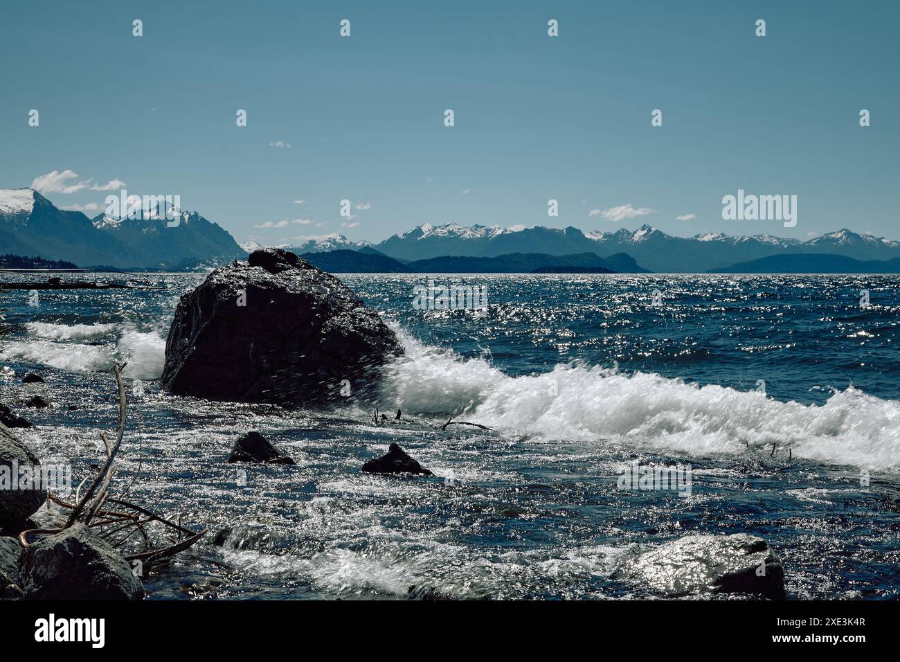 Malerische felsige Berge in einem türkisfarbenen See. Wellen schaumen um einen riesigen Stein. Wolken in einem klaren blauen Himmel. Stockfoto