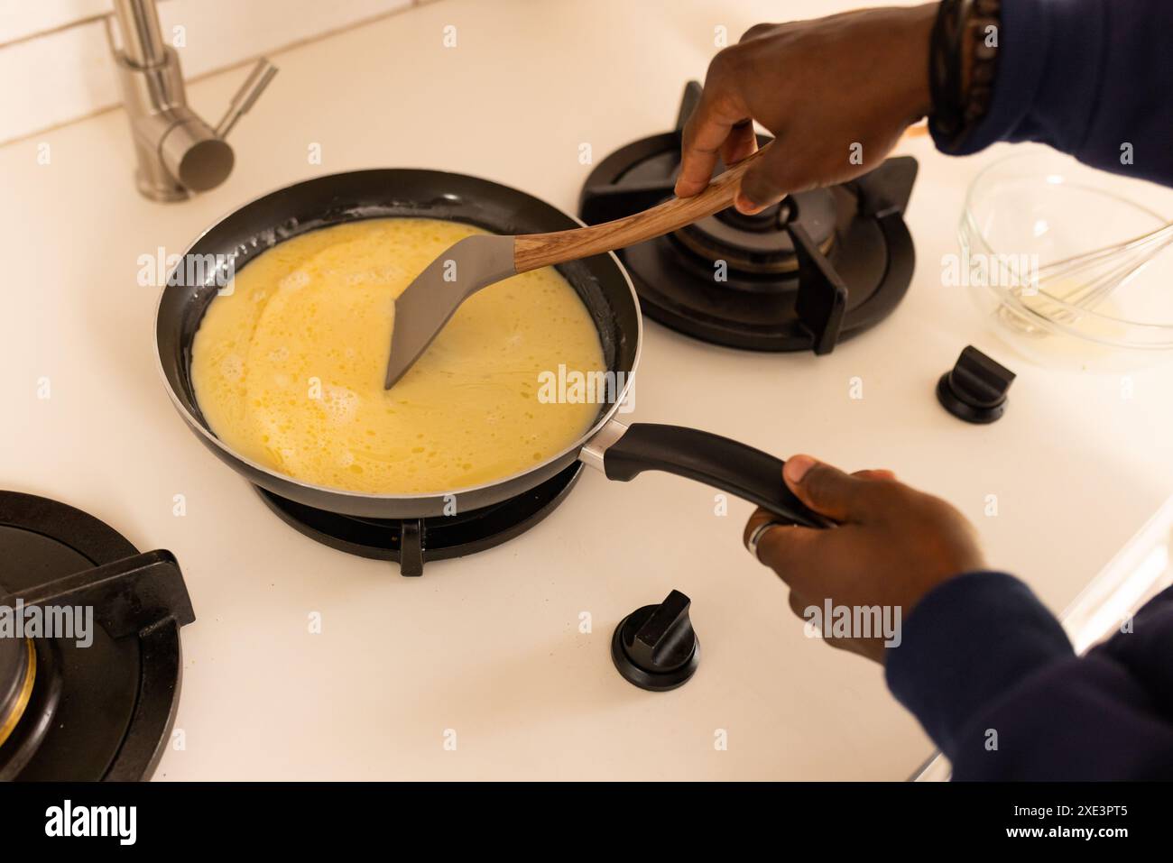 Zu Hause, kochen Frühstück, afroamerikanischer Mann, der Eier in der Pfanne auf dem Herd rührt Stockfoto
