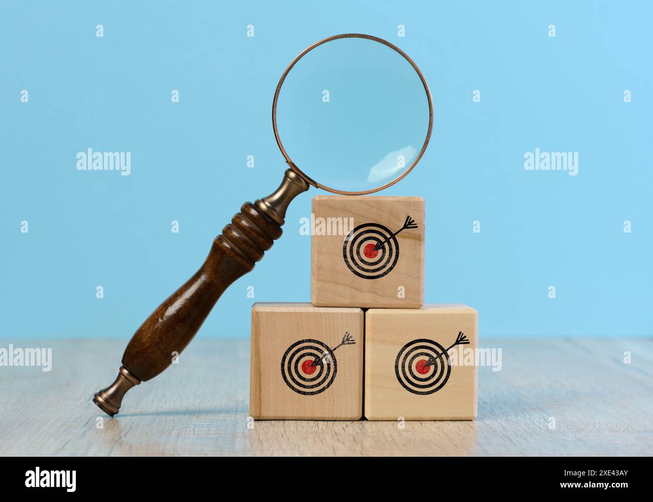 Holzwürfel mit gezeichnetem Ziel und einer Lupe auf blauem Hintergrund, die die Suche nach Wahrheit symbolisiert Stockfoto