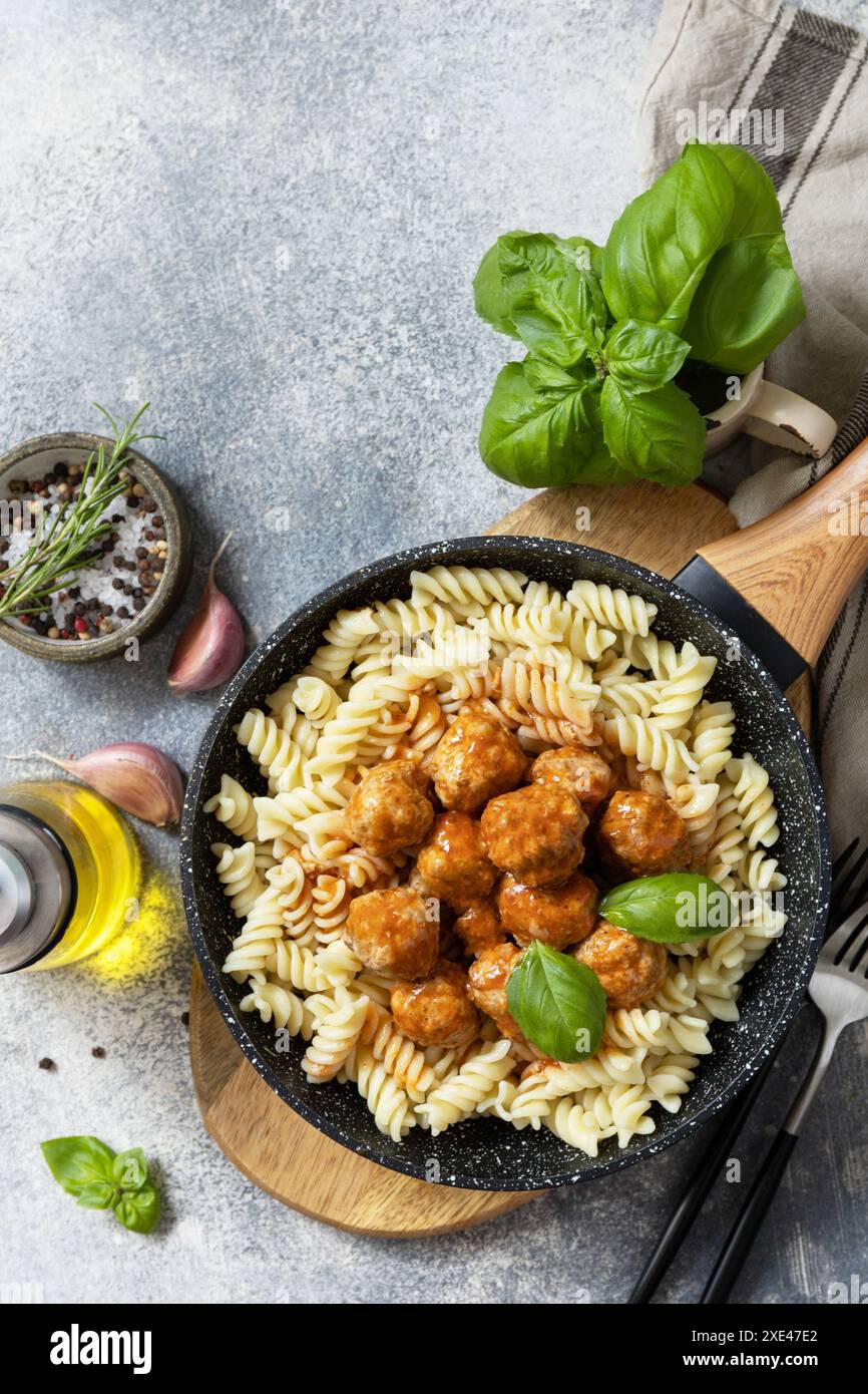 Italienische Küche. Italienische Fusilli-Pasta mit Fleischbällchen in Tomatensauce und Basilikum auf grauem Steingrund. Flach liegend, Draufsicht. Stockfoto