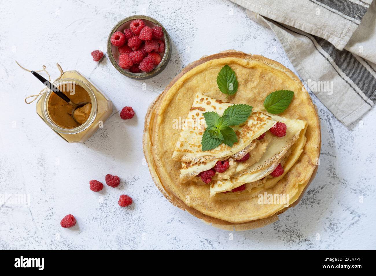 Gesundes Frühstück, Pancake Day. Köstliche hausgemachte Crepes mit Himbeeren und Erdnusspaste auf einer Steinplatte. Oben Stockfoto