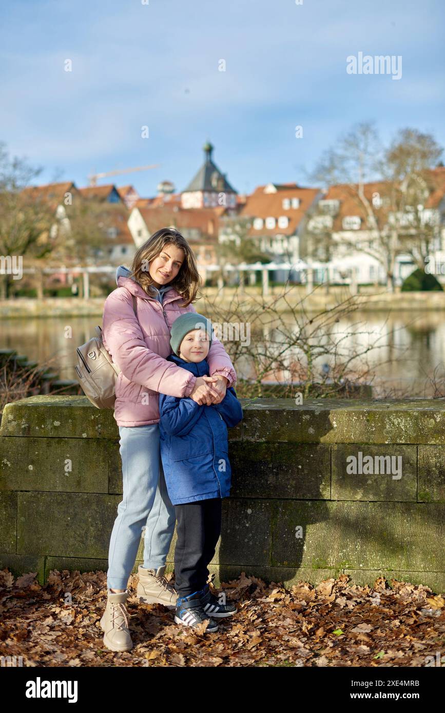 Riverside Family Harmony: Mutter, 30 Jahre alt, und Sohn - schöner 8-jähriger Junge, stehend am Neckar River und Historic Half-T Stockfoto