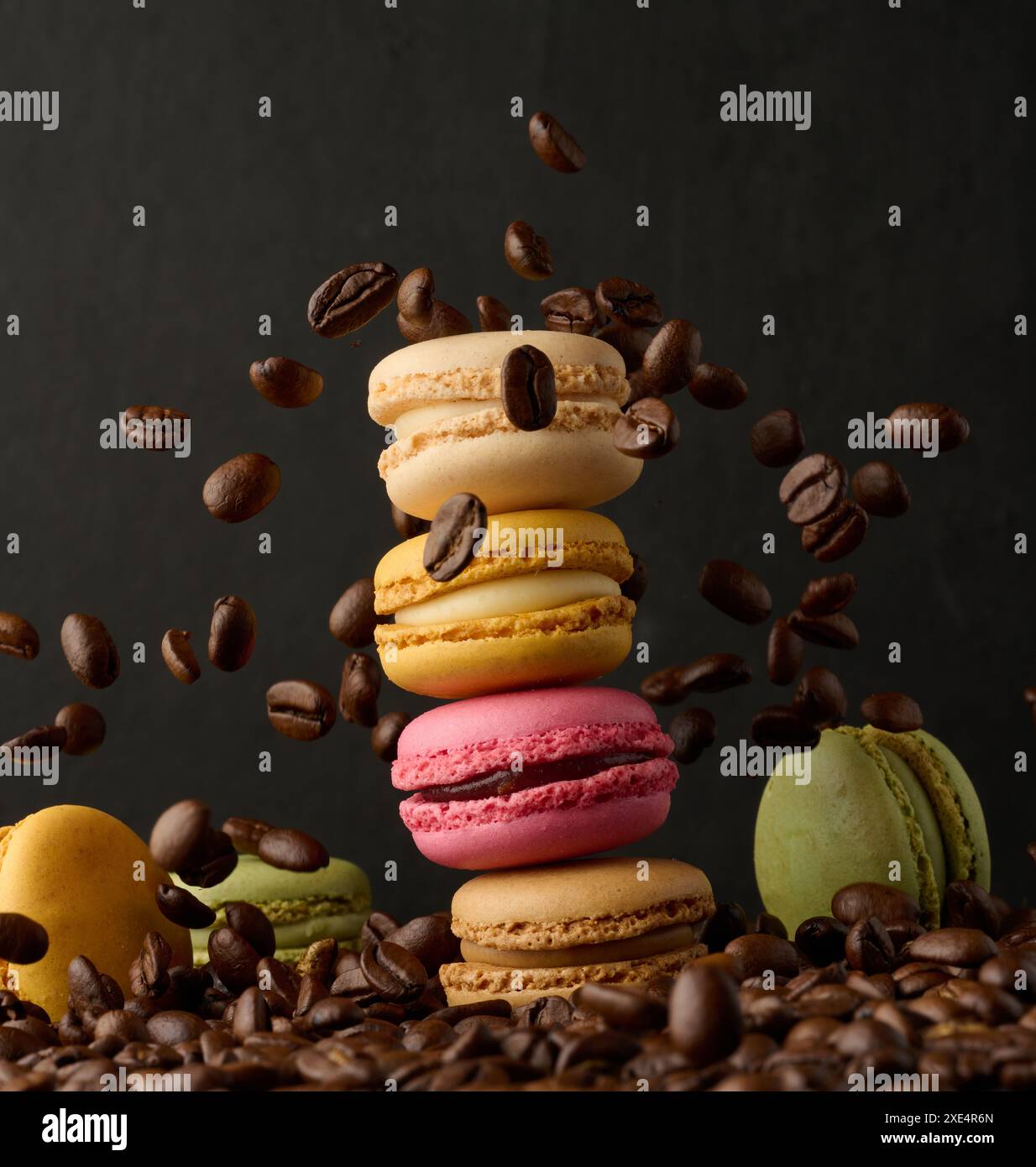 Stapel bunter Macarons und fliegende Kaffeebohnen auf schwarzem Hintergrund Stockfoto