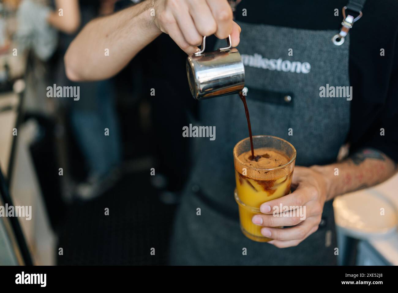 Zugeschnittene Aufnahme eines nicht erkennbaren Barista-Mannes, der Eiskaffee mit frischem Orangensaft im Glas zubereitet. Nahaufnahme der Kellnerin im Café, die Kaffee serviert Stockfoto
