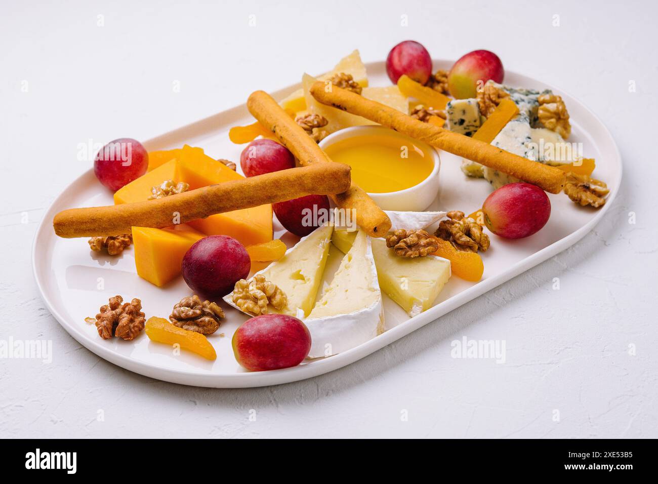 Käseplatte mit Honig, Nüssen und roten Trauben Stockfoto