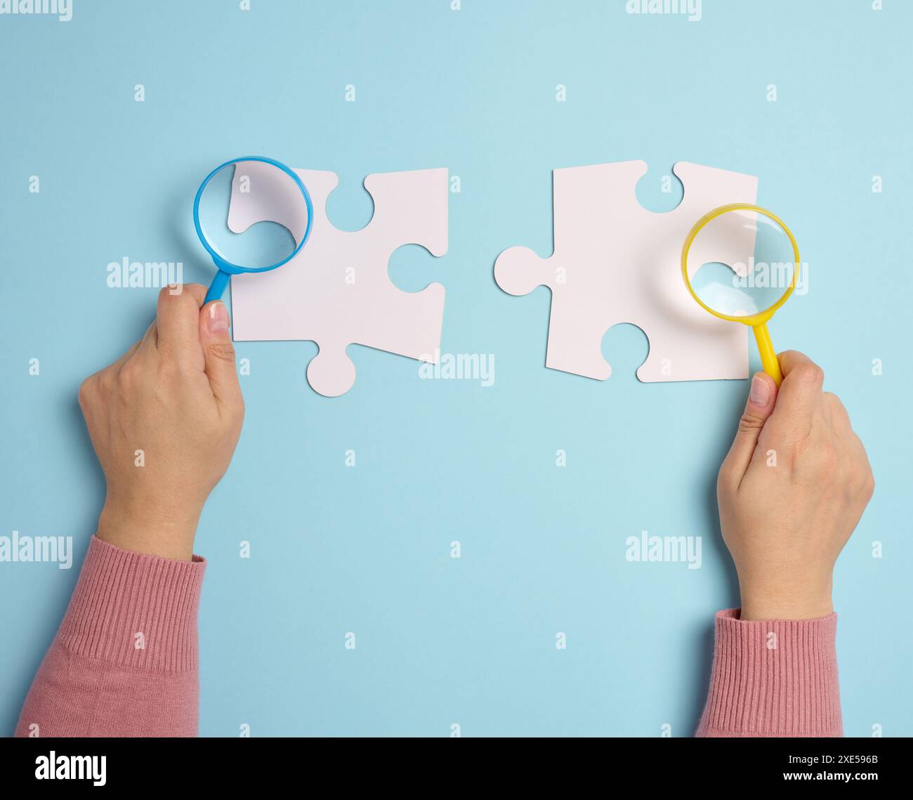 Weiße leere Puzzles und eine Lupe in der Hand auf blauem Hintergrund Stockfoto