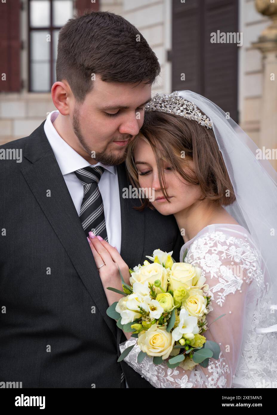 Hochzeitsporträt eines jungen, schönen, modernen Paares. Der Bräutigam umarmt die Braut, sie klammerte sich an ihn und hielt einen Strauß weißer Rosen. Berühren, Liebe, Fühlen Stockfoto