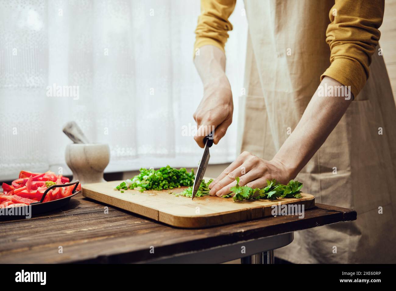 Unerkennbarer Mann, der Koriander mit Küchenmesser in der Küche hackt Stockfoto