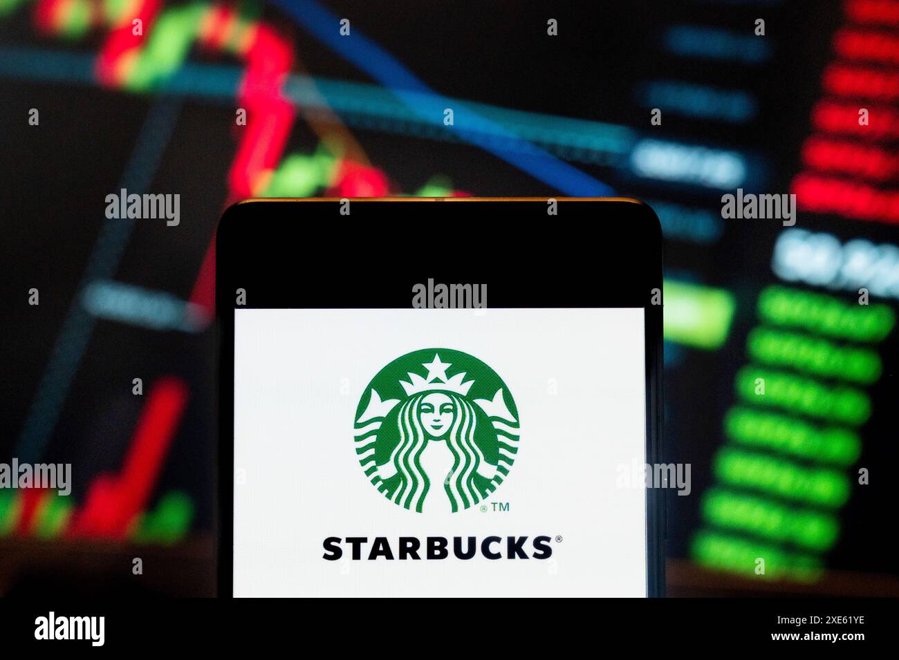 In dieser Fotoabbildung wird das Logo der amerikanischen multinationalen Kette Starbucks Coffee (NASDAQ: SBUX) auf einem Smartphone mit einem Index der wirtschaftlichen Börsen im Hintergrund dargestellt. Stockfoto