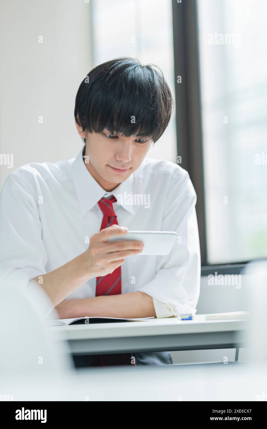 Männlicher Schüler, der im Klassenzimmer ein Smartphone ansieht Stockfoto