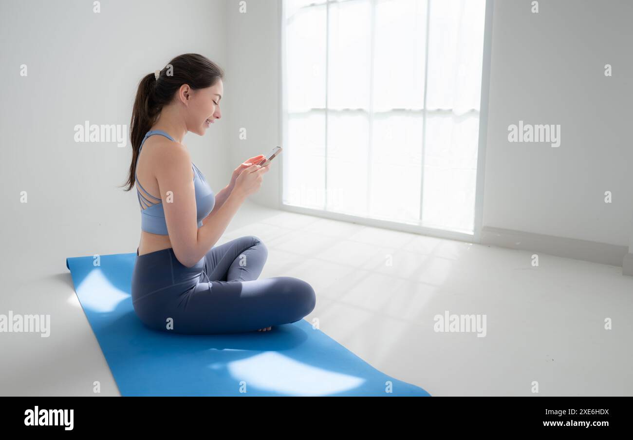 Junge sportliche Frauen sitzen auf Yogamatten und schauen auf ihr Smartphone. Stockfoto