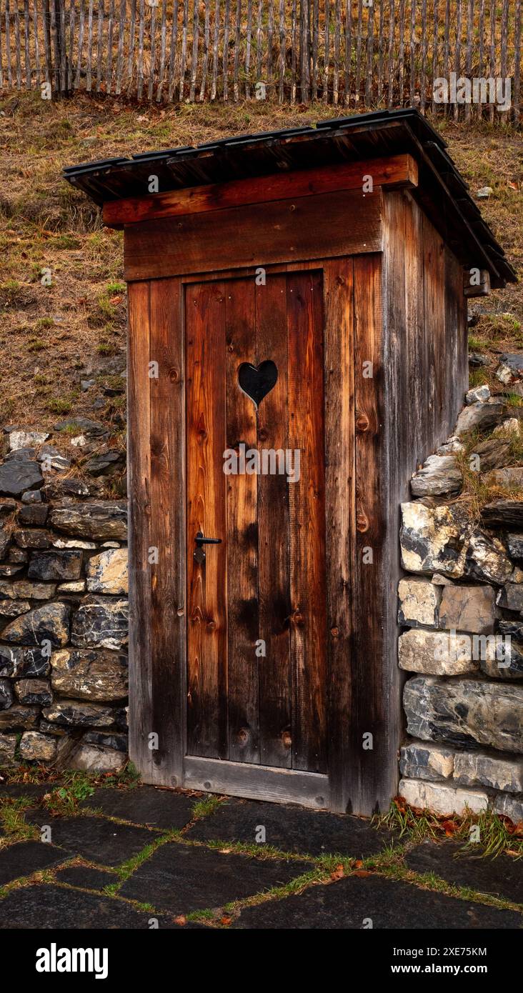 Ein Bild einer alten Außentoilette befindet sich an einer Steinmauer in einem Hang Stockfoto