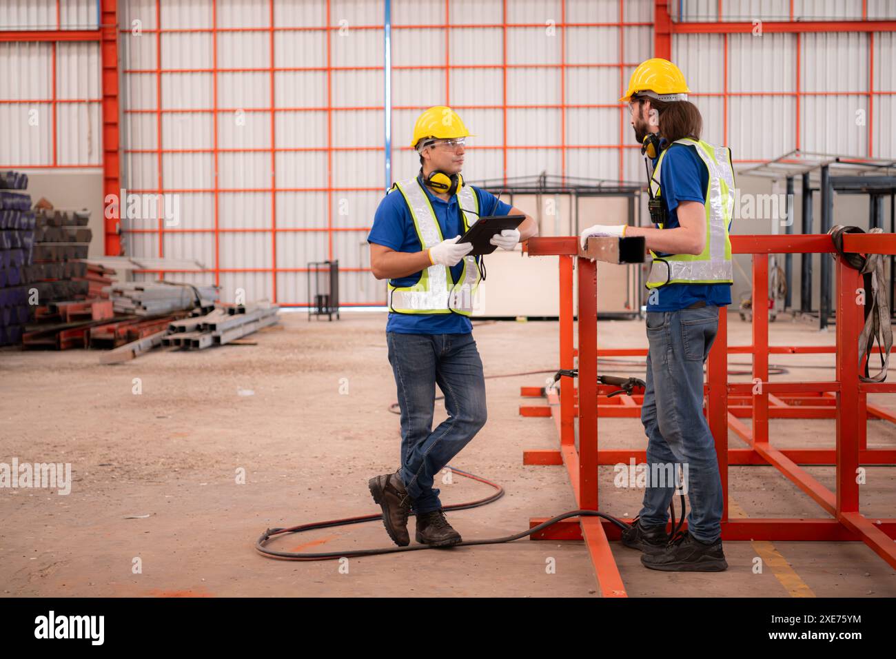 Porträt von zwei Arbeitern mit digitalem Tablet-Ständer vor der roten Stahlkonstruktion Stockfoto