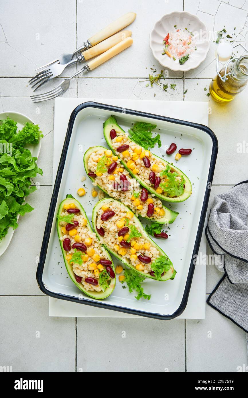 Zucchini gefüllt mit Petitim, roten Bohnen, Mais mit Basilikum und Soße, gebacken auf einem alten, zerrissenen Fliesenhintergrund. Draufsicht. Stockfoto