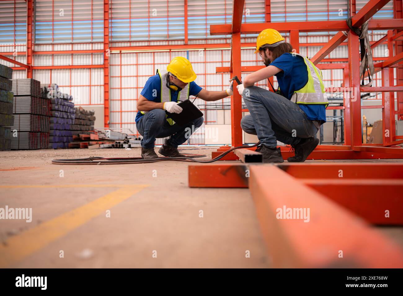Porträt von zwei Arbeitern, die ein digitales Tablet verwenden, vor der roten Stahlkonstruktion Stockfoto