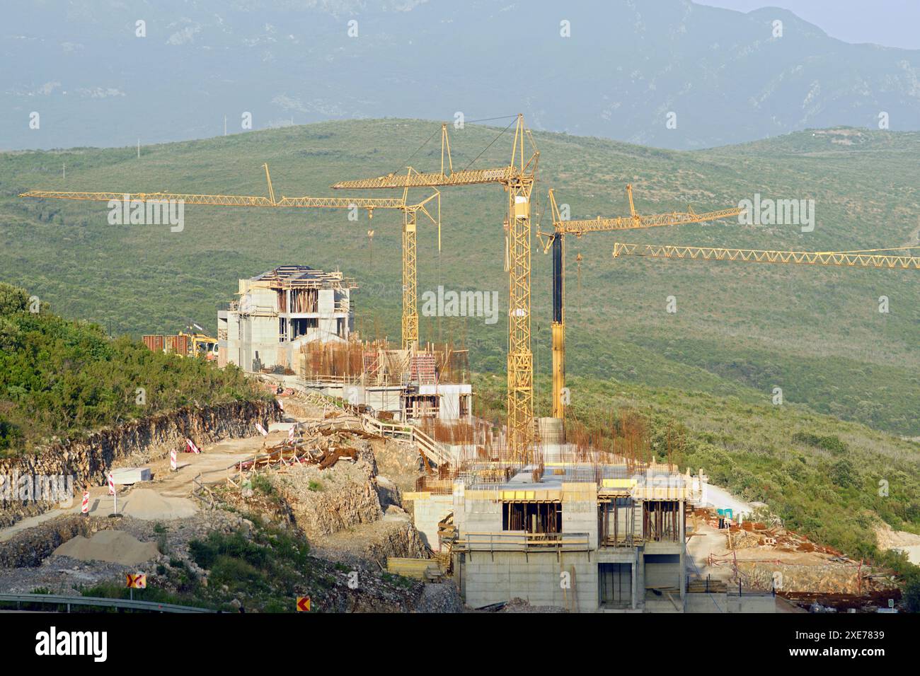 Blick auf die Baustelle: Betonhäuser und drei große Turmkräne vor dem Hintergrund von Bergen und Grün Stockfoto