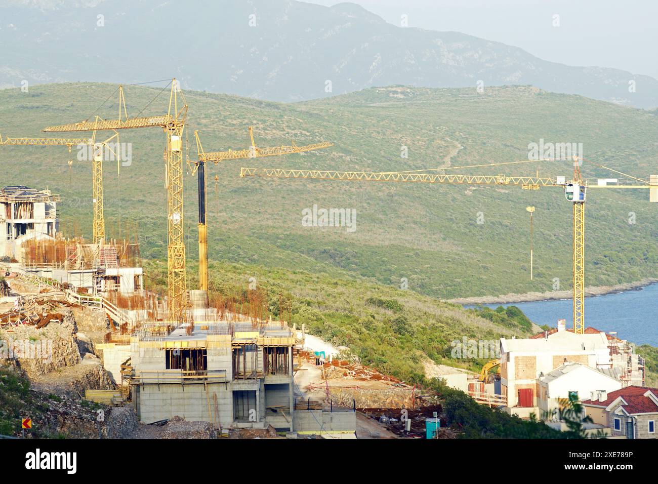 Blick auf die Baustelle: Mehrere Turmkräne und Betonvillen vor dem Hintergrund grüner Berge Stockfoto